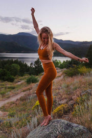 The Conservationist: Eco-friendly turmeric leggings made out of post consumer recycled plastic. Lifestyle image of woman wearing leggings in the mountains. 
