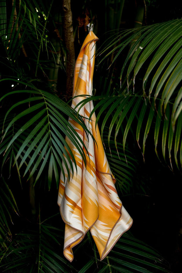 Image of yellow, salmon, white and gold eco-friendly tribal pattern towel hanging up in a tree. Available for purchase on The Conservationist.